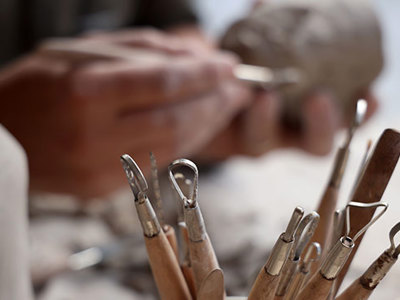 Hands shaping a clay sculpture with pottery tools in the foreground.